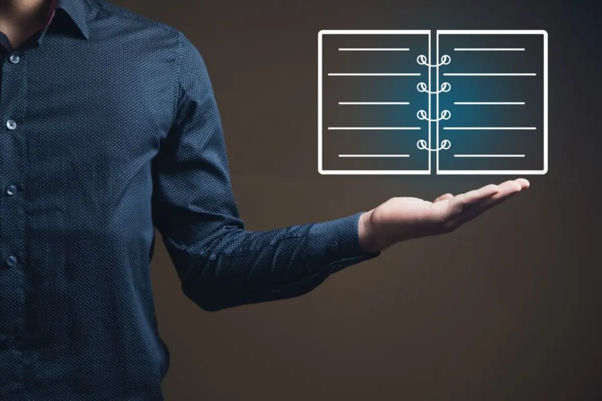 A person in a blue polka-dot shirt holds out a hand with a glowing, illustrated open notebook floating above it.