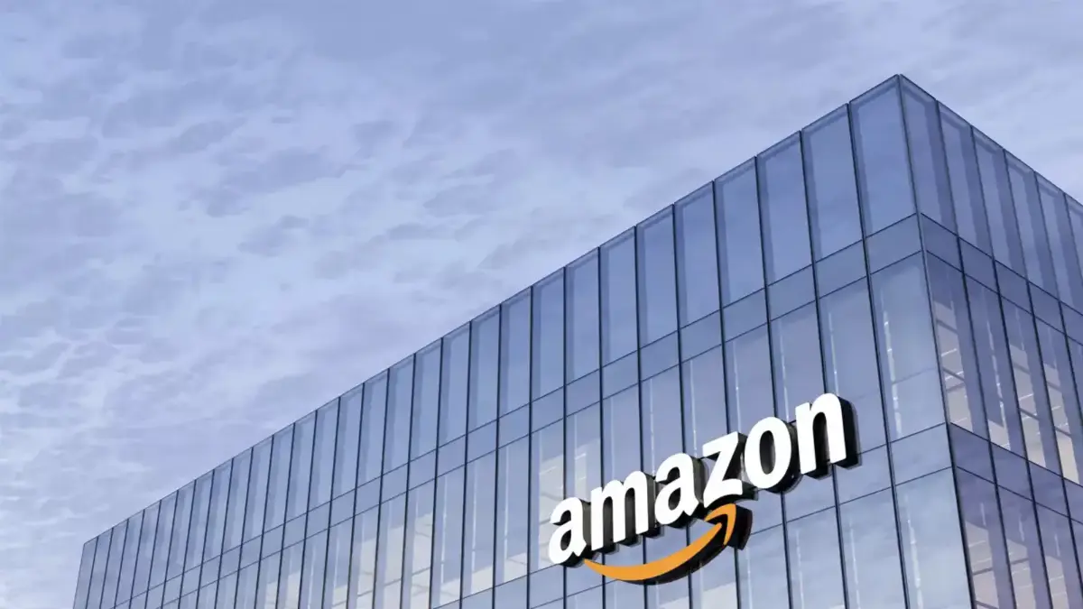 The Amazon logo displayed on a modern glass building against a cloudy blue sky.