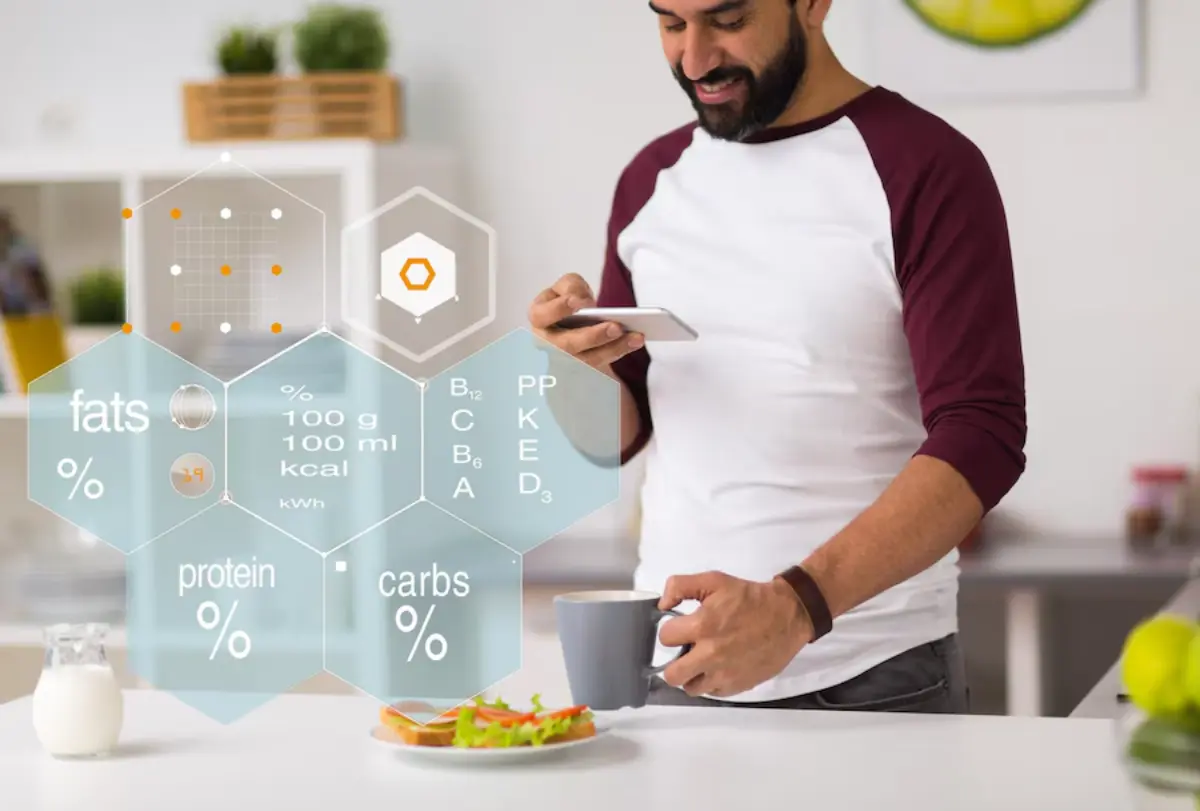 A man in a kitchen holds a smartphone and a coffee mug, surrounded by nutritional information and a plate of salad.