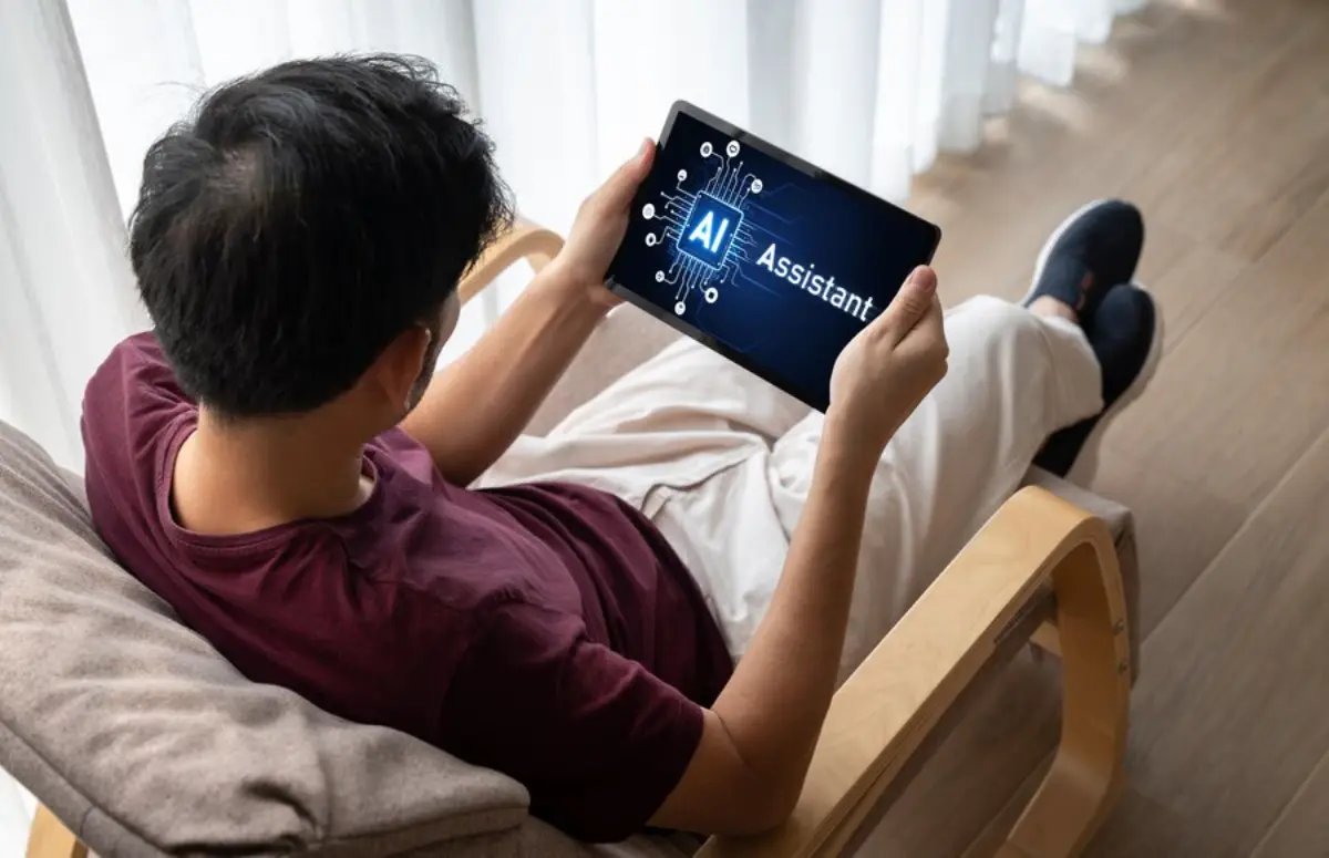 A person sitting on a chair, looking at a tablet displaying AI Assistant with a circuit design in a bright room.