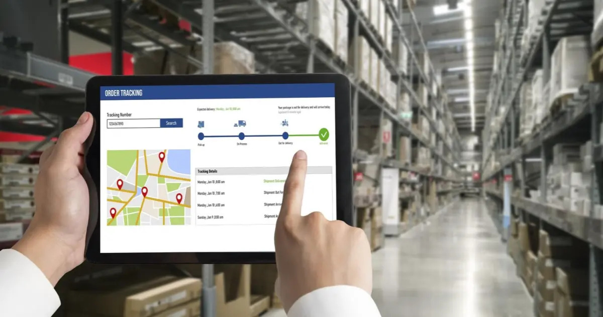 A person uses a tablet displaying an order tracking interface in a warehouse, indicating delivery status and tracking details.