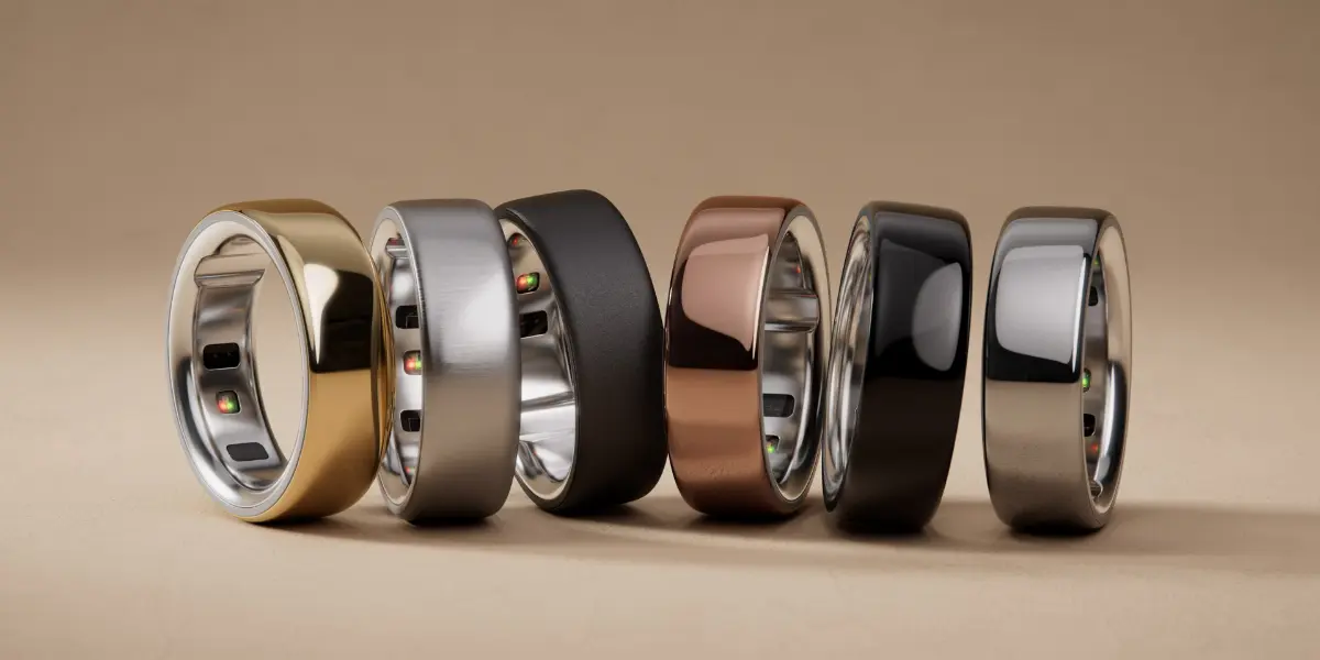 A collection of six sleek, modern rings in gold, silver, black, bronze, and grey, displayed against a soft brown background.