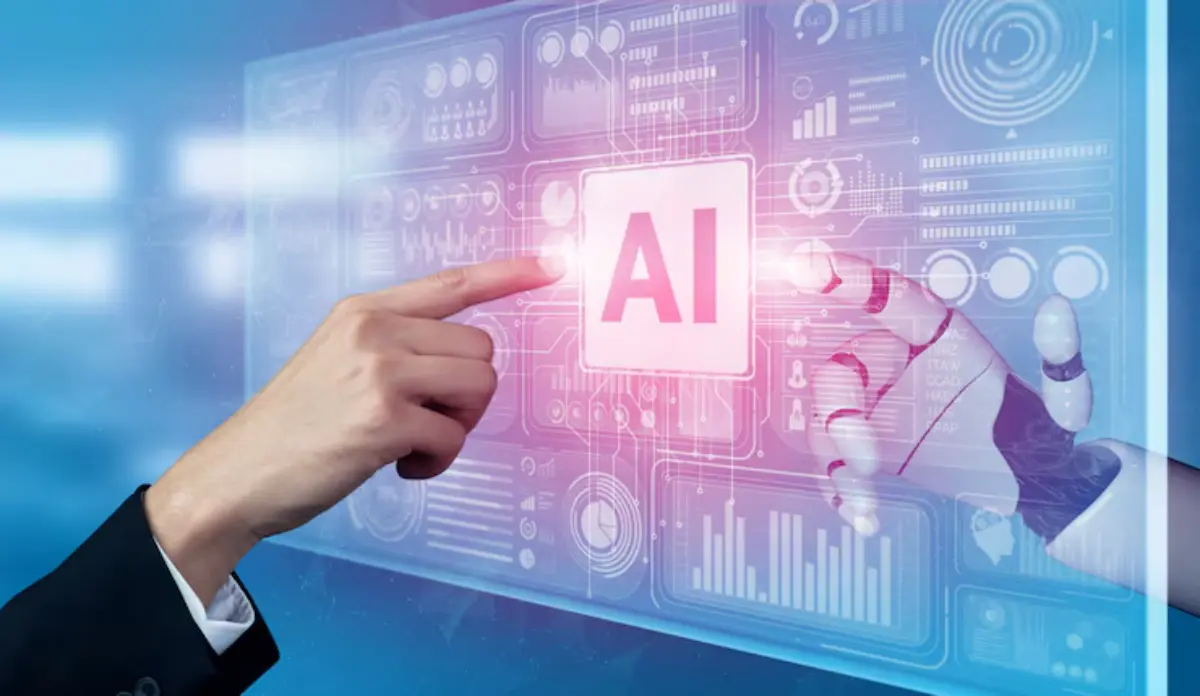 A human hand and a robotic hand touch a glowing AI button on a digital interface, symbolizing interaction between humans and technology.