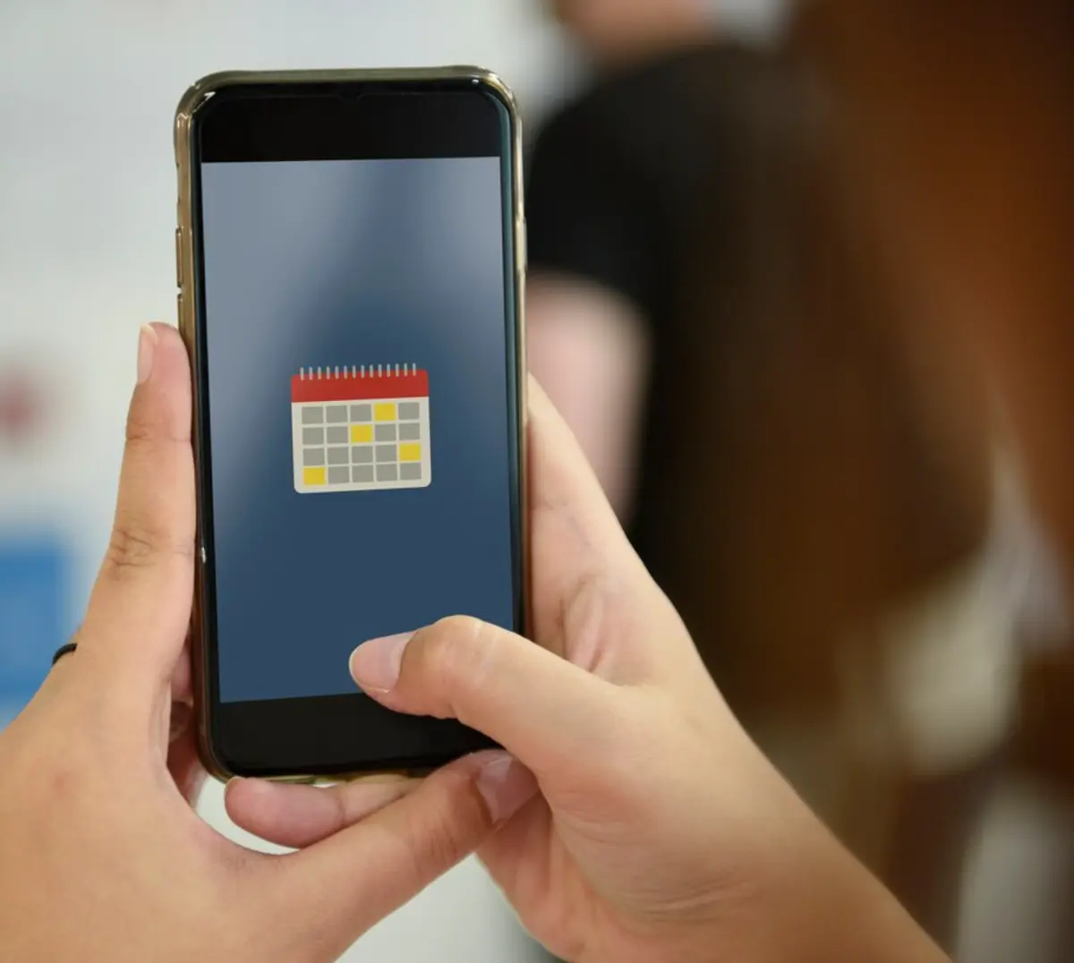A person holds a smartphone displaying a calendar app icon on a blue background.
