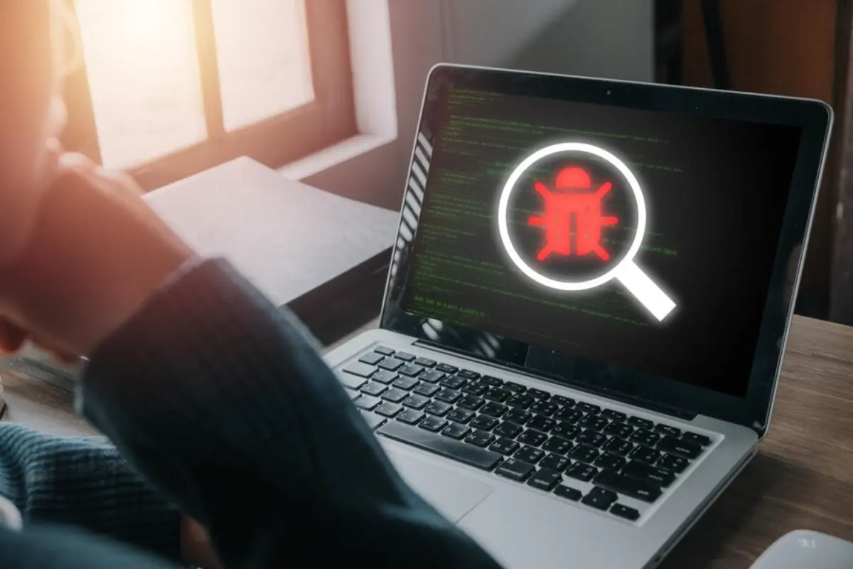 A person examines a laptop displaying a red bug icon and code on the screen, symbolizing computer debugging or troubleshooting.