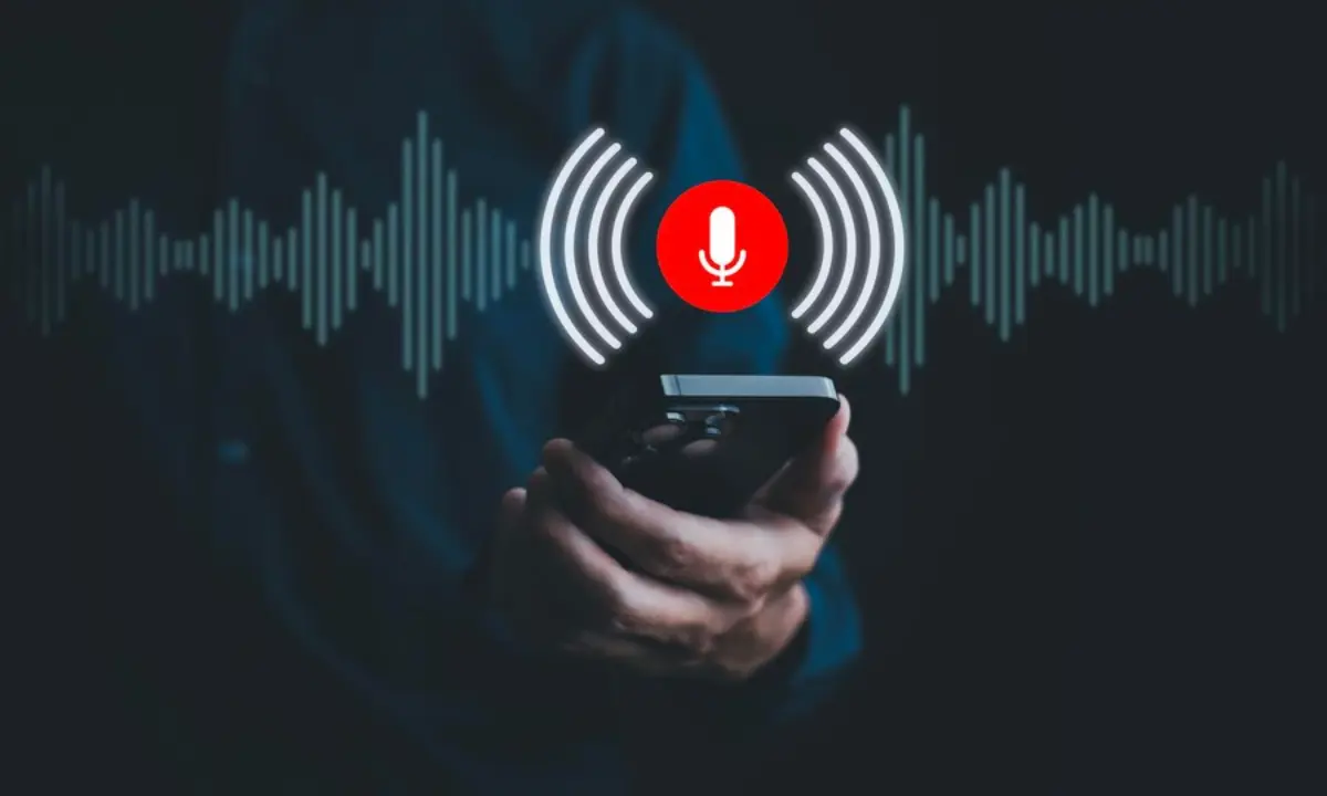 A person holding a smartphone with a red microphone icon and sound waves, indicating voice recording in a dark background.