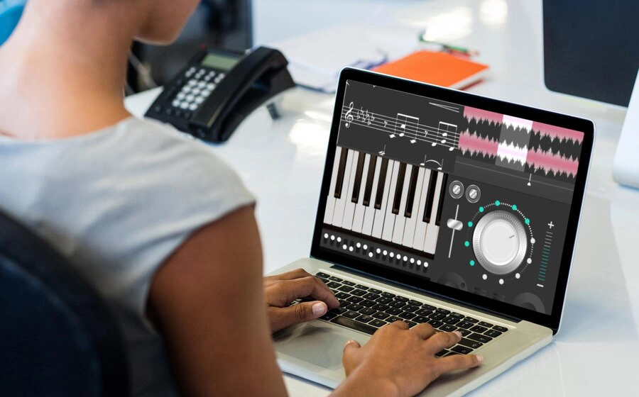 A person using a laptop with a digital music production interface, featuring a keyboard, audio waveform, and control knobs.