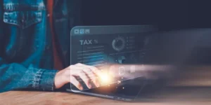 A person typing on a laptop with a digital overlay displaying tax data and charts, symbolizing online tax preparation.