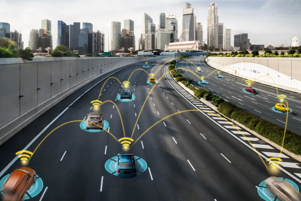 Aerial view of a smart highway with connected cars, displaying communication signals amid a modern city skyline.