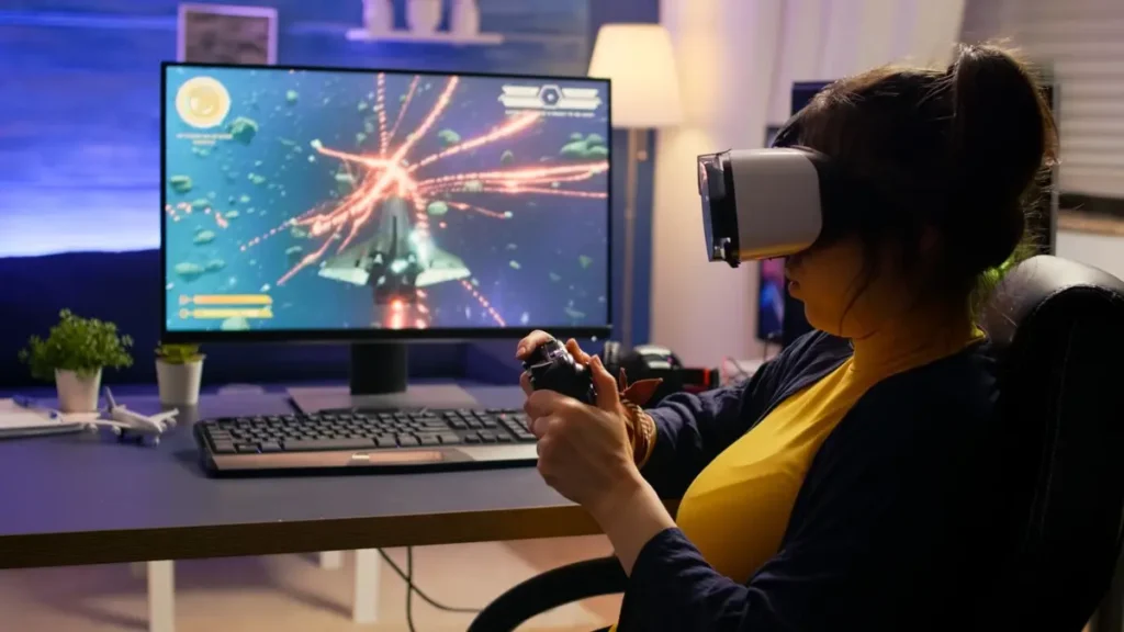 A person wearing a virtual reality headset holds a game controller, focused on a gaming monitor displaying an action-packed space scene.